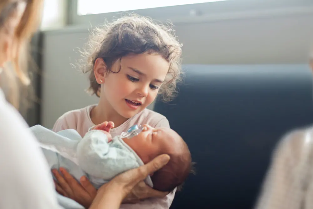 Frau hält Baby auf dem Arm und zeigt es einem Mädchen