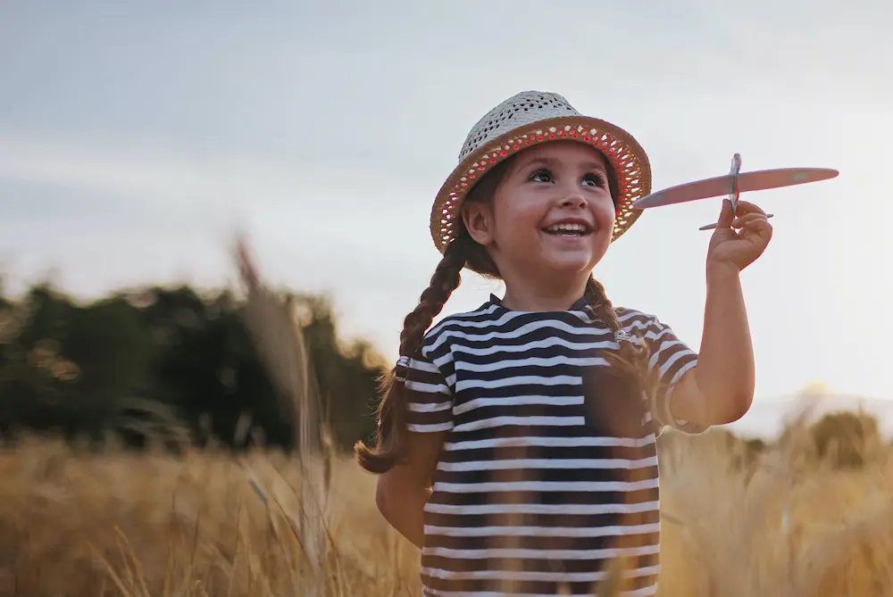 Mädchen mit kleinem Modellflugzeug steht auf einem Kornfeld und lacht